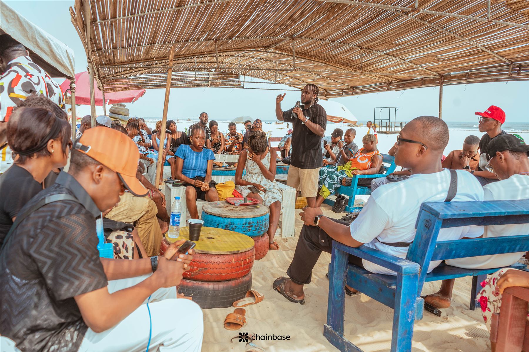 Asian Dickson hosting Chainbase Beachfest, addressing the crowd on the microphone under the beach canopy