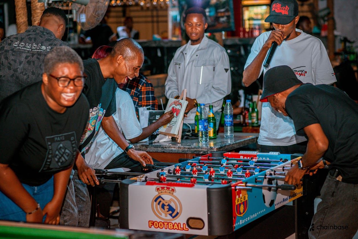 Guests playing table football at the Chainbase Mixer Party, a host on the microphone in the background