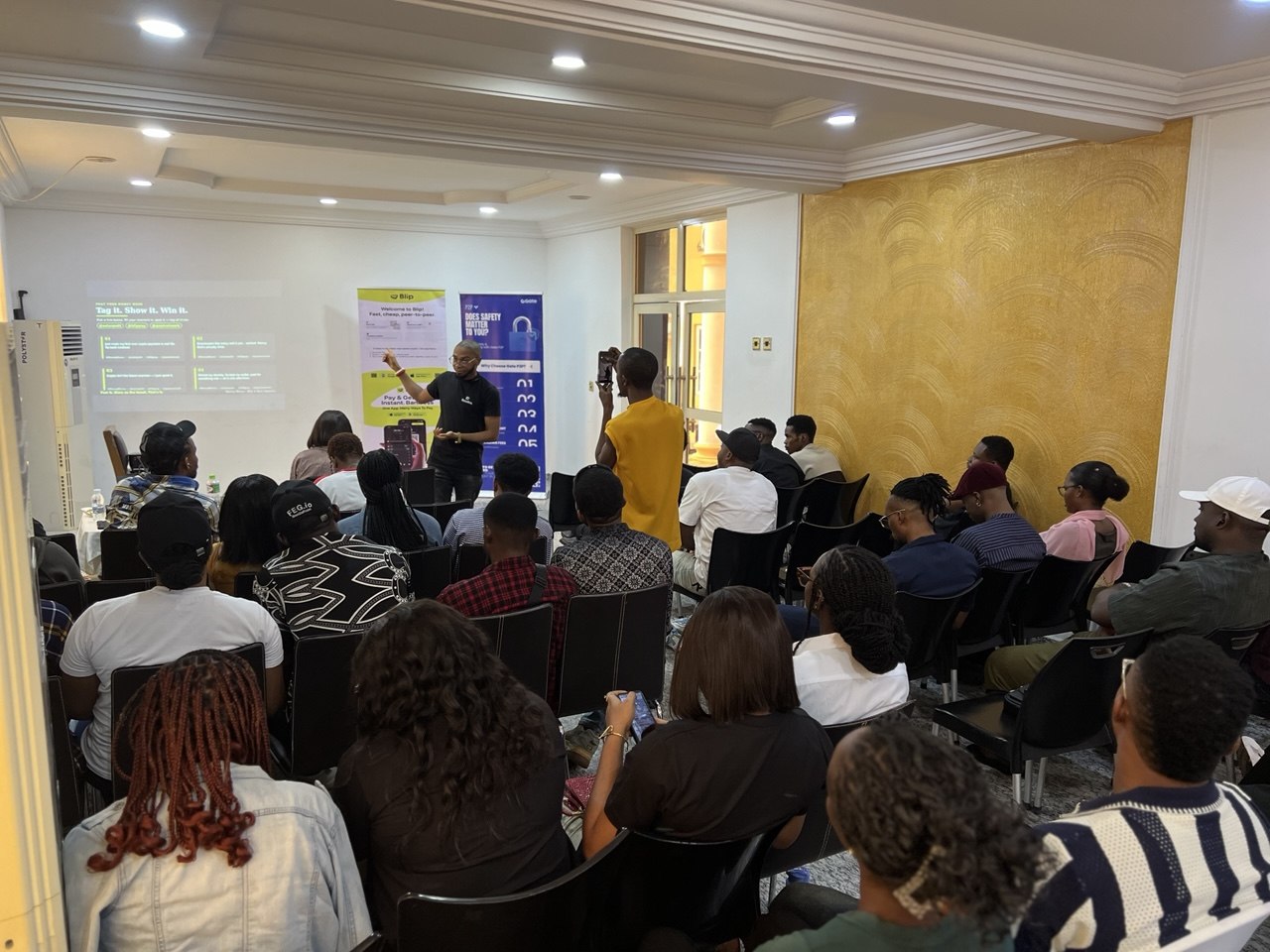 Wide view of the Money Moves Uyo session, presenter at the screen with a full seated room, Blip and Quai Network banners either side